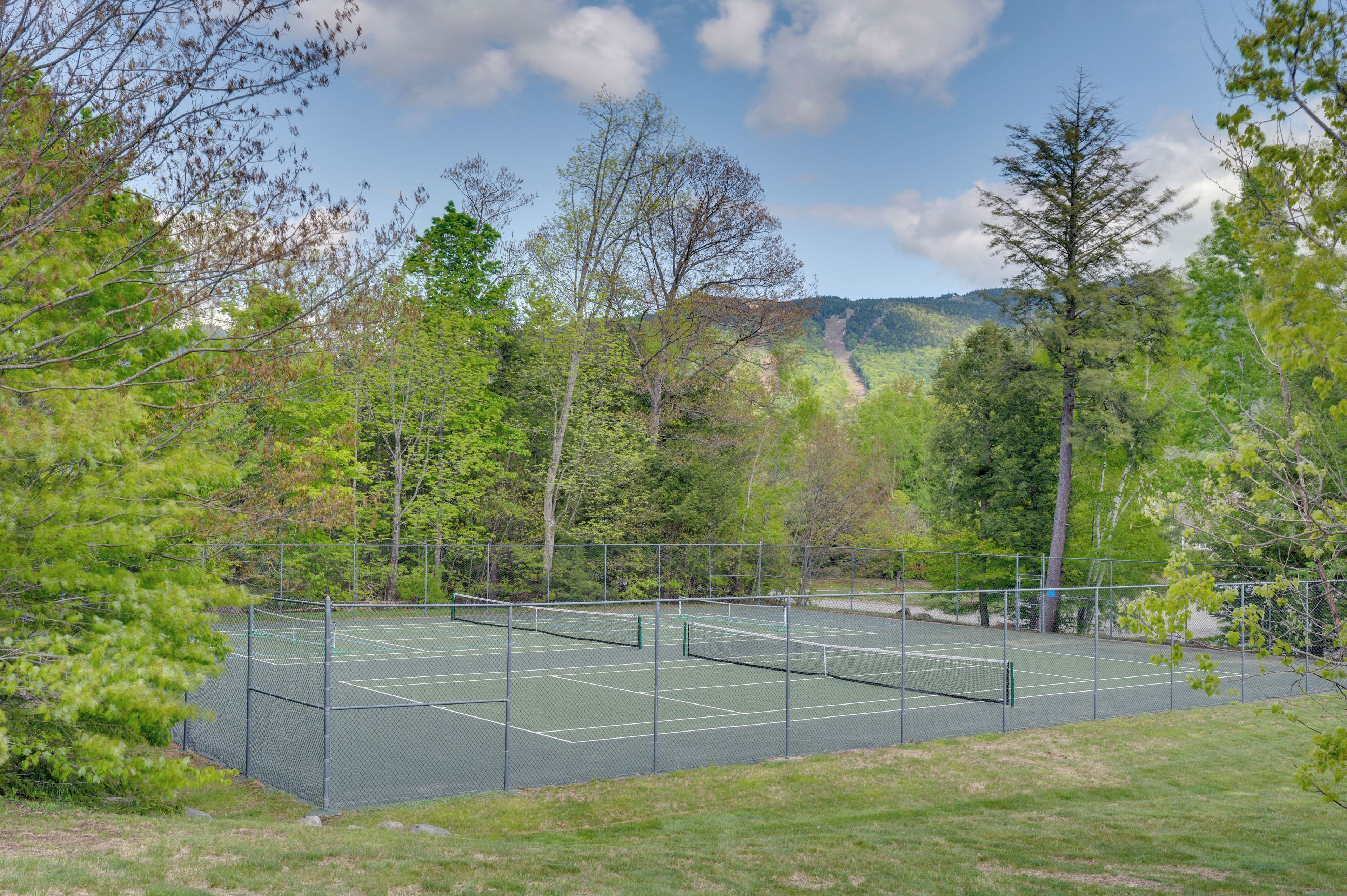 Una cancha de tenis rodeada de árboles y una montaña al fondo.