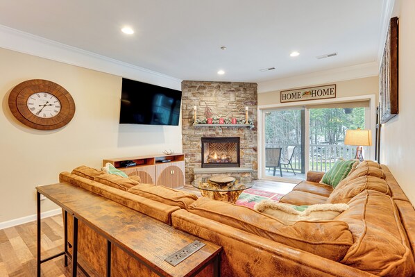 A cozy living room with a stone fireplace, a large sectional sofa, a wooden coffee table, and a flat-screen TV mounted on the wall. - Relaxing Lincoln Condo w/ Fireplace & Shuttle (Lincoln)