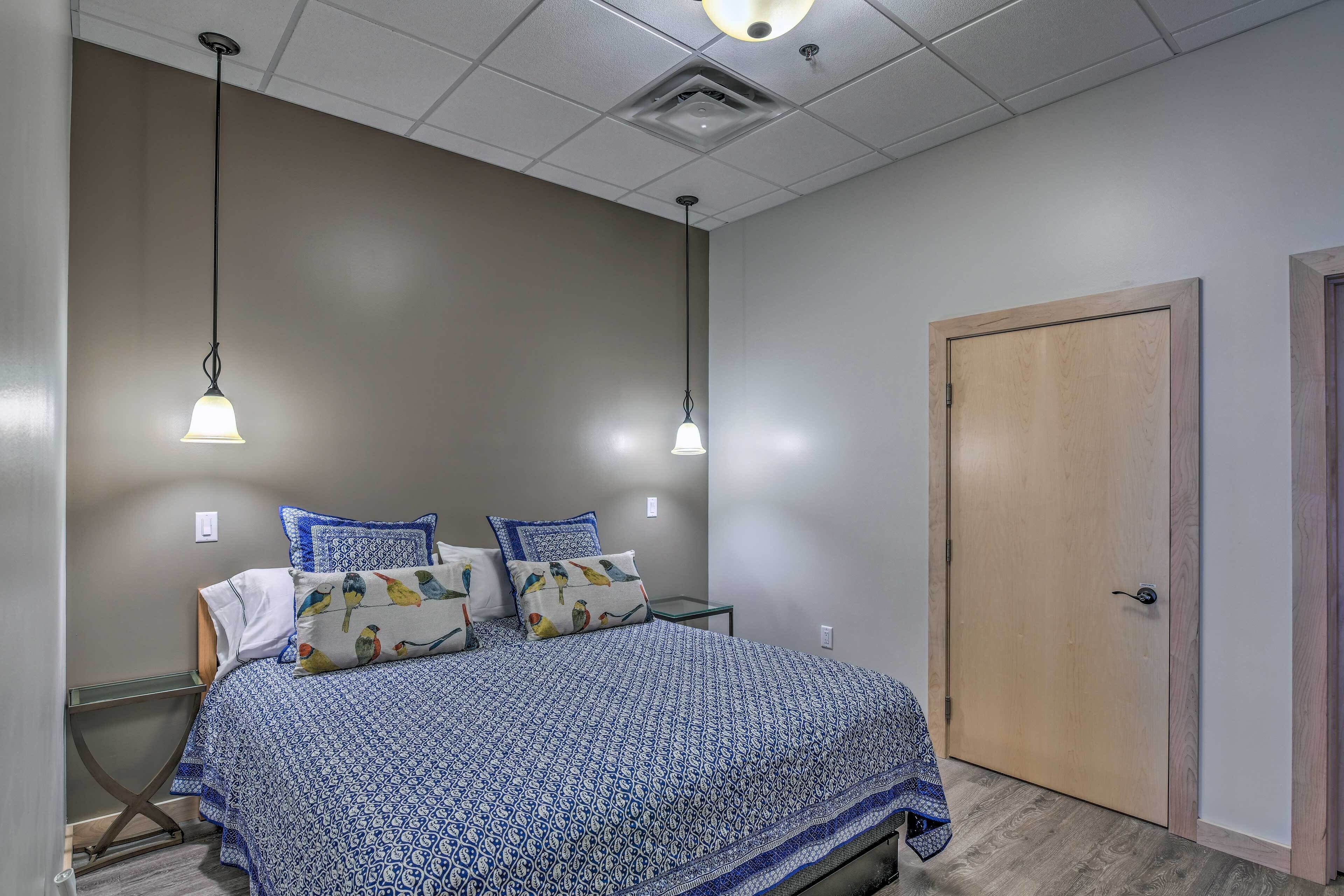 A bedroom with a bed, two bedside lamps, a wooden door, and a small table.