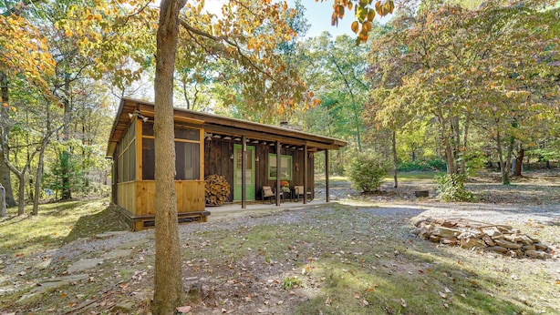 A rustic cabin with a covered porch, surrounded by trees and a gravel path.