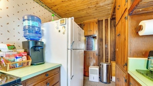 A compact kitchen with a water dispenser, a refrigerator, wooden cabinets, and a trash bin.