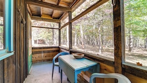 A rustic cabin with a wooden interior, a table with a bowl, and large windows overlooking a forest.