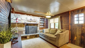 A cozy living room with a stone fireplace, a wooden bench, a sofa, and a bookshelf.