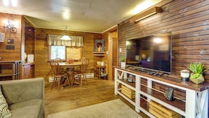 A cozy, wood-paneled room with a dining area, a sofa, and a TV mounted on a wooden wall.