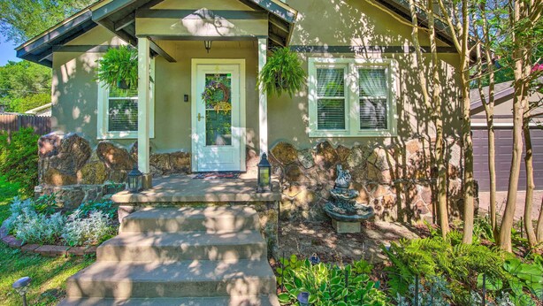 A house with a front porch, stone steps, a decorative door, and a small garden with plants and a birdbath.