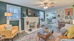 A living room with a fireplace, sofa, coffee table, and a view into the kitchen.