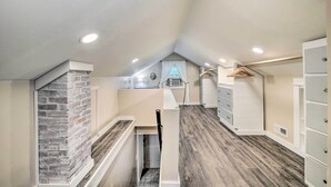 A narrow hallway with a brick accent wall, a white staircase, and a small window with white curtains.