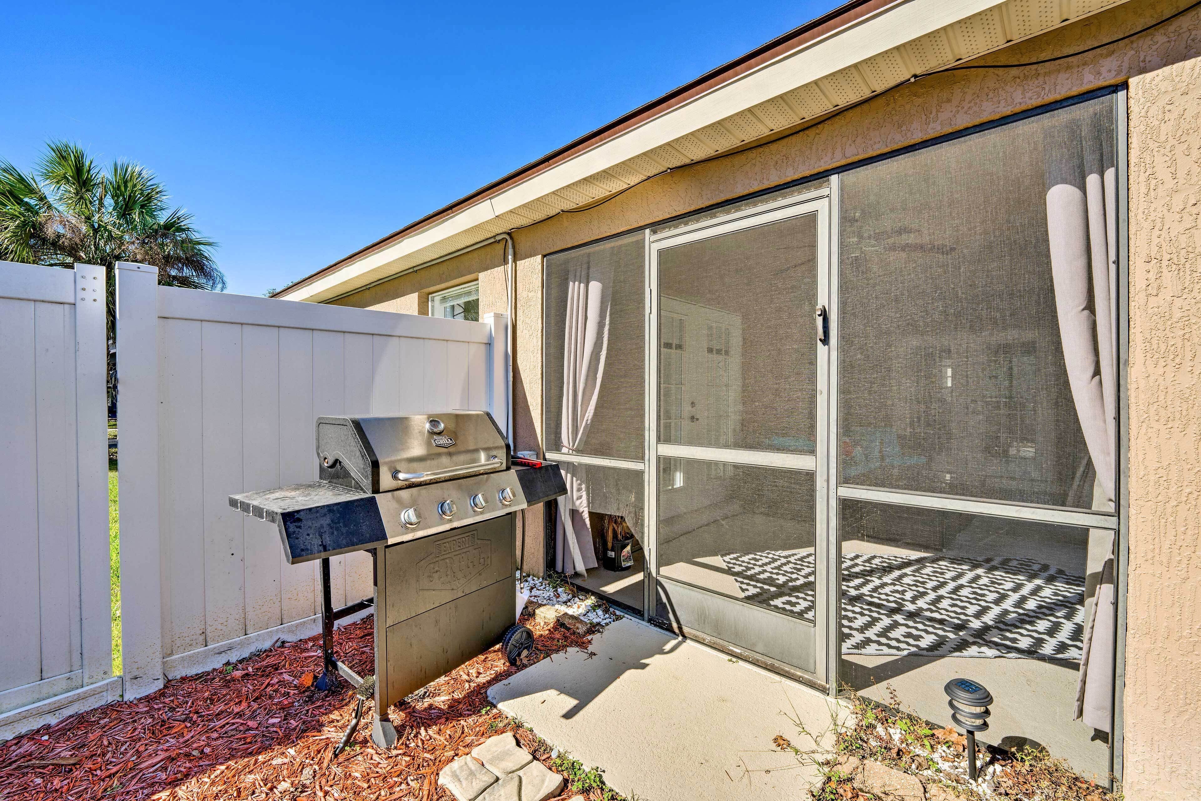 A backyard with a barbecue grill, a sliding glass door, and a white fence.