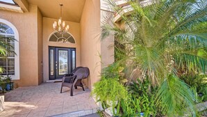 A covered patio with a chair, a door, and lush greenery. - Clermont Vacation Rental w/ Pool: 11 Mi to Disney (Clermont)