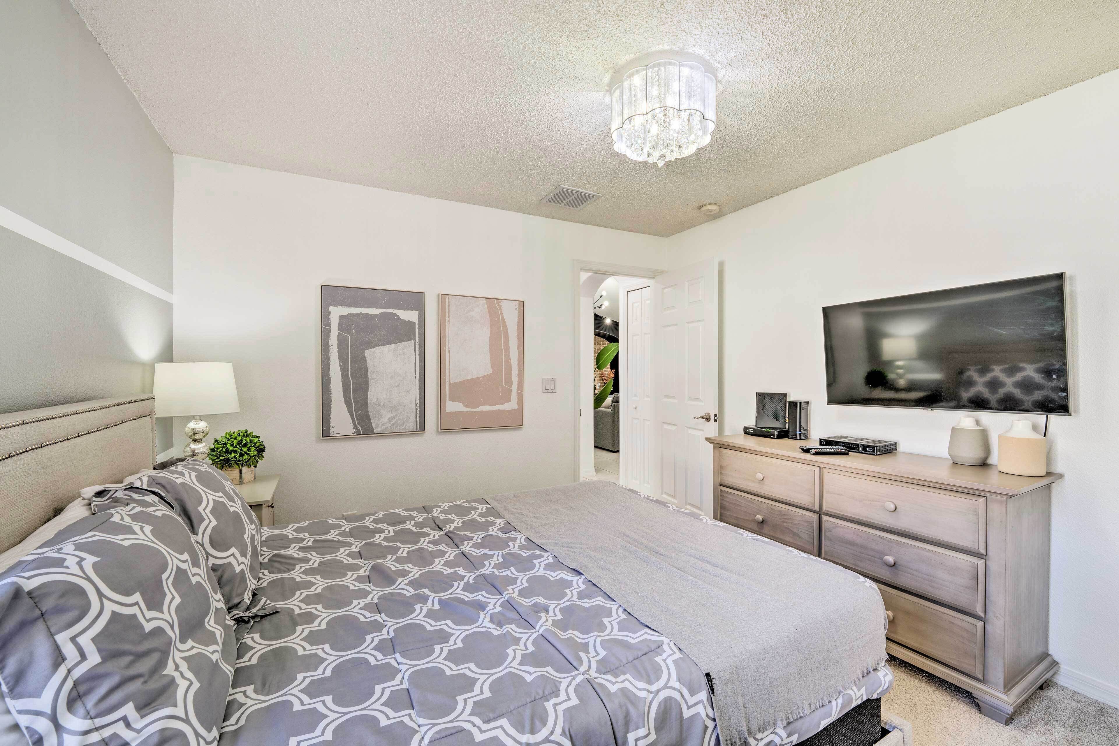 A bedroom with a bed, a dresser, a TV, and artwork on the wall.