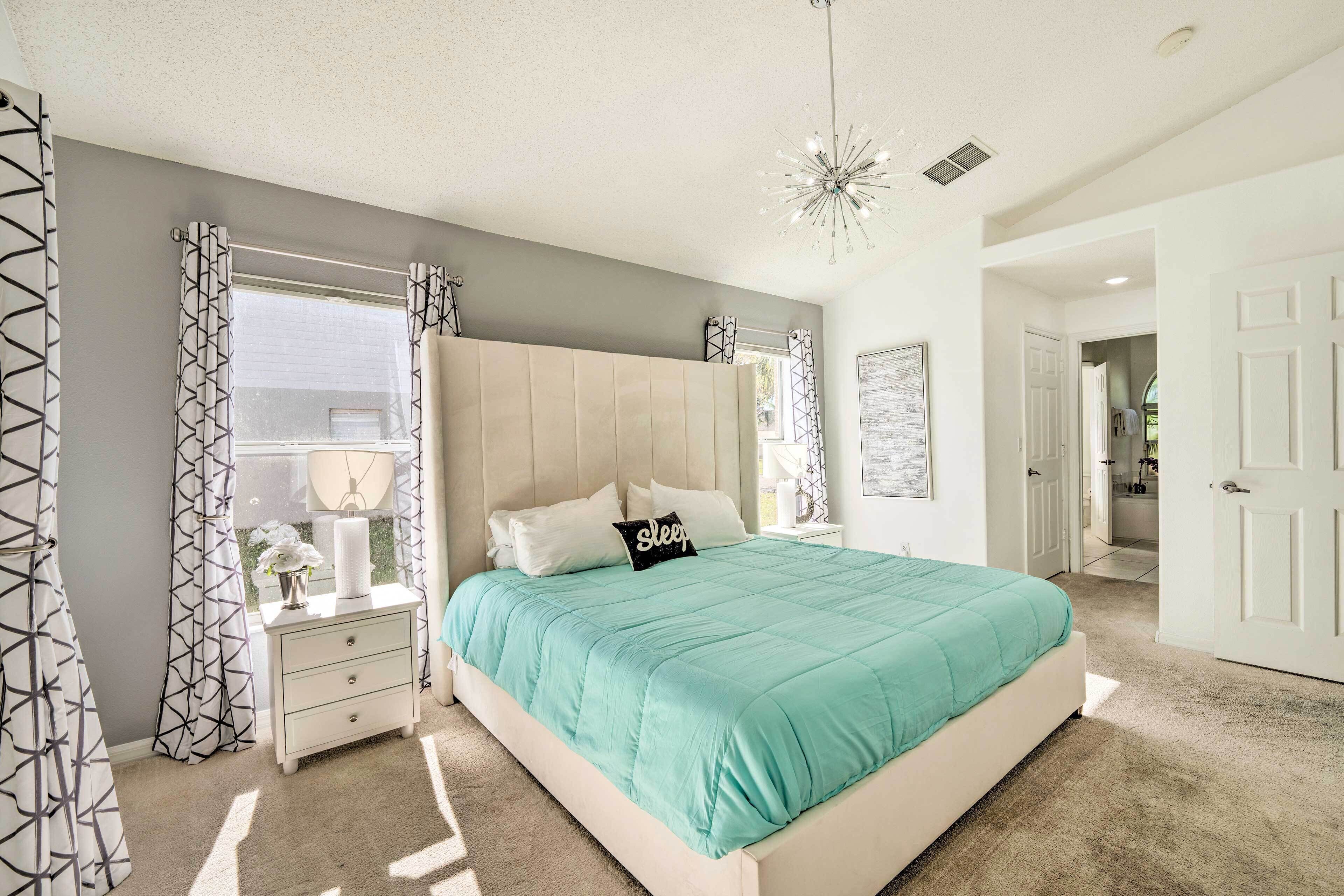 A bedroom with a bed, nightstands, a dresser, a window with curtains, and a chandelier.