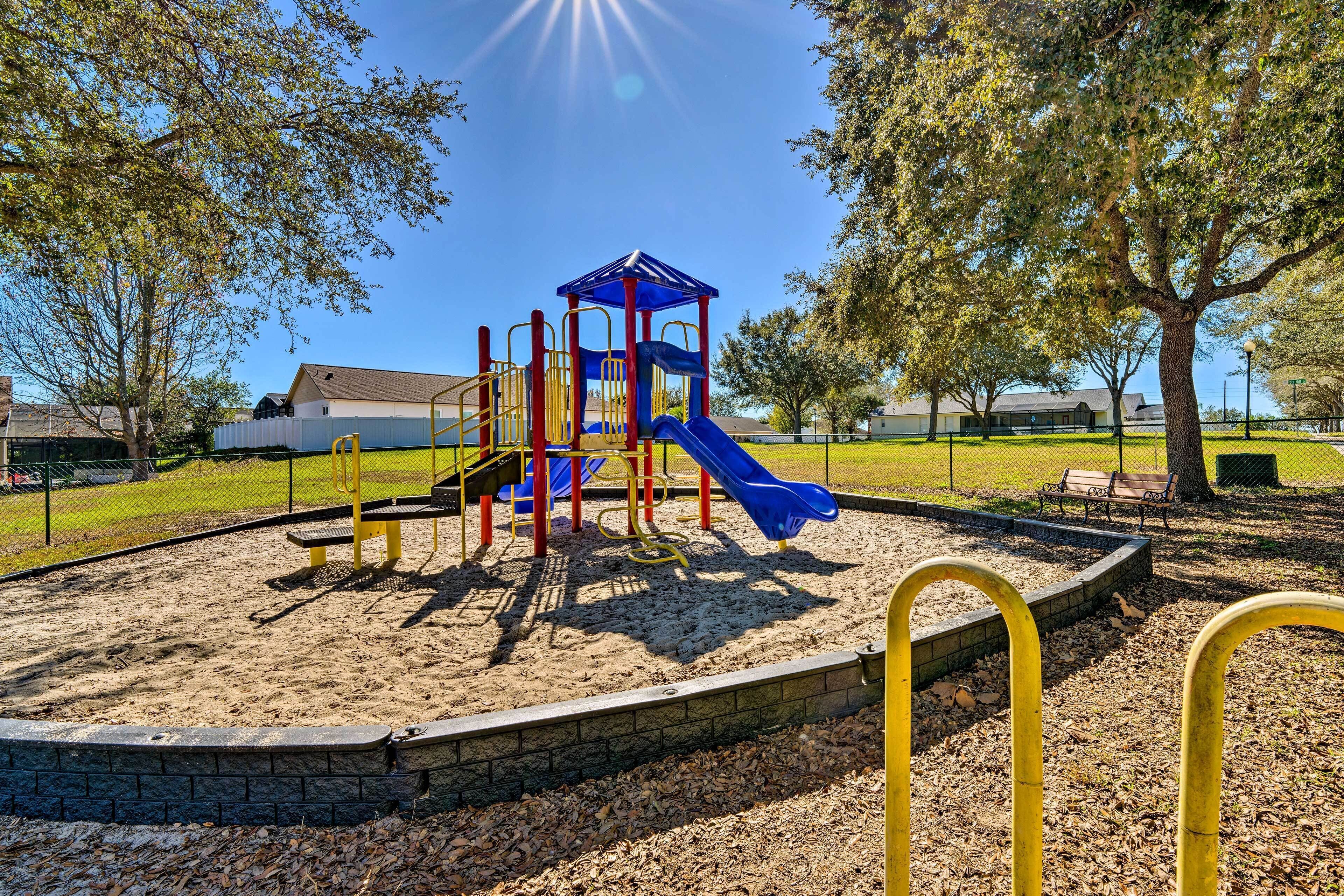 Ein Spielplatz mit einer blauen Rutsche und Klettergerüsten, umgeben von Bäumen und einem Zaun.