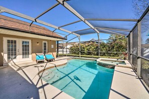 A covered outdoor swimming pool with lounge chairs and a house in the background.