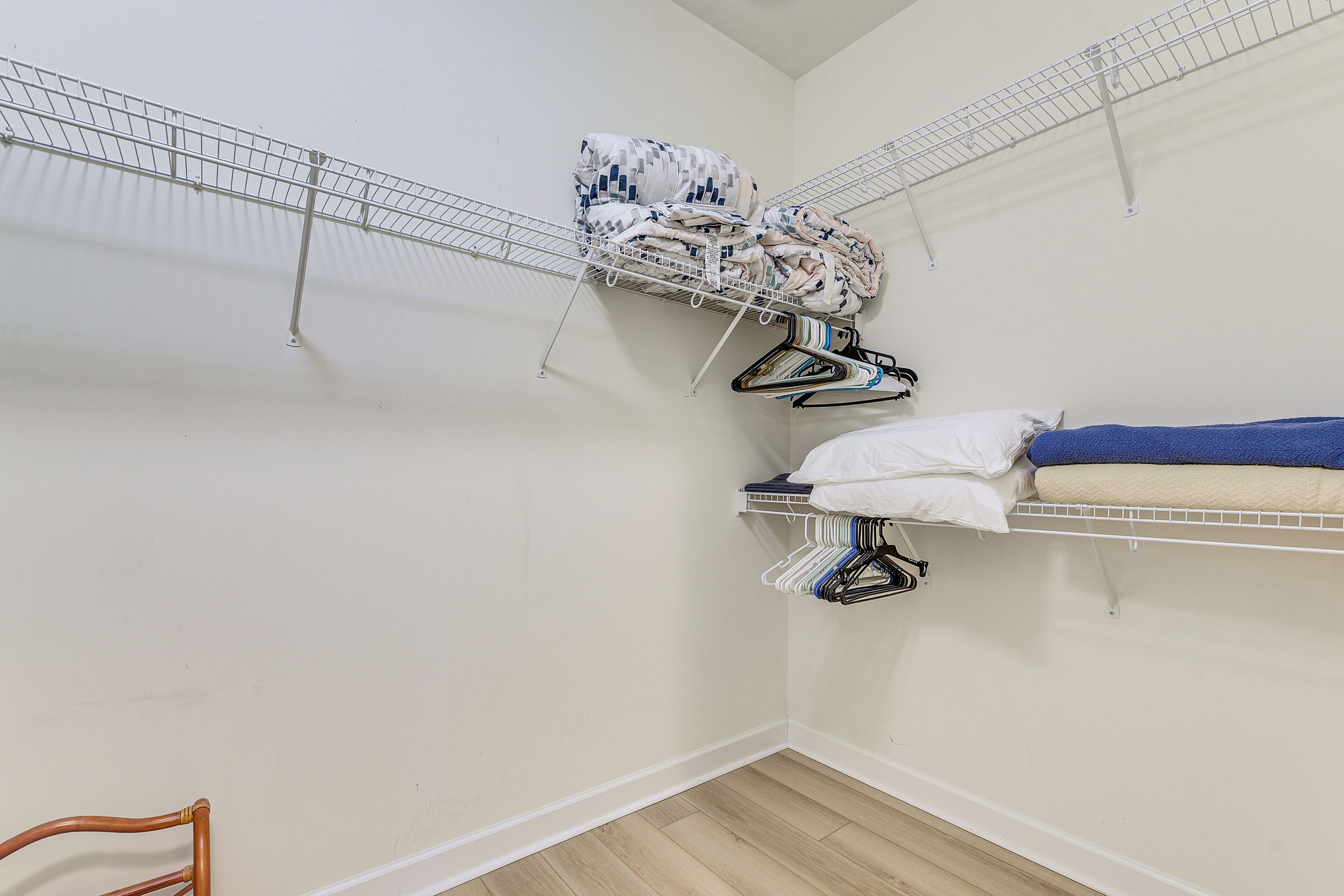 A small room with two metal wire shelves, one holding folded clothes and the other with hanging clothes.