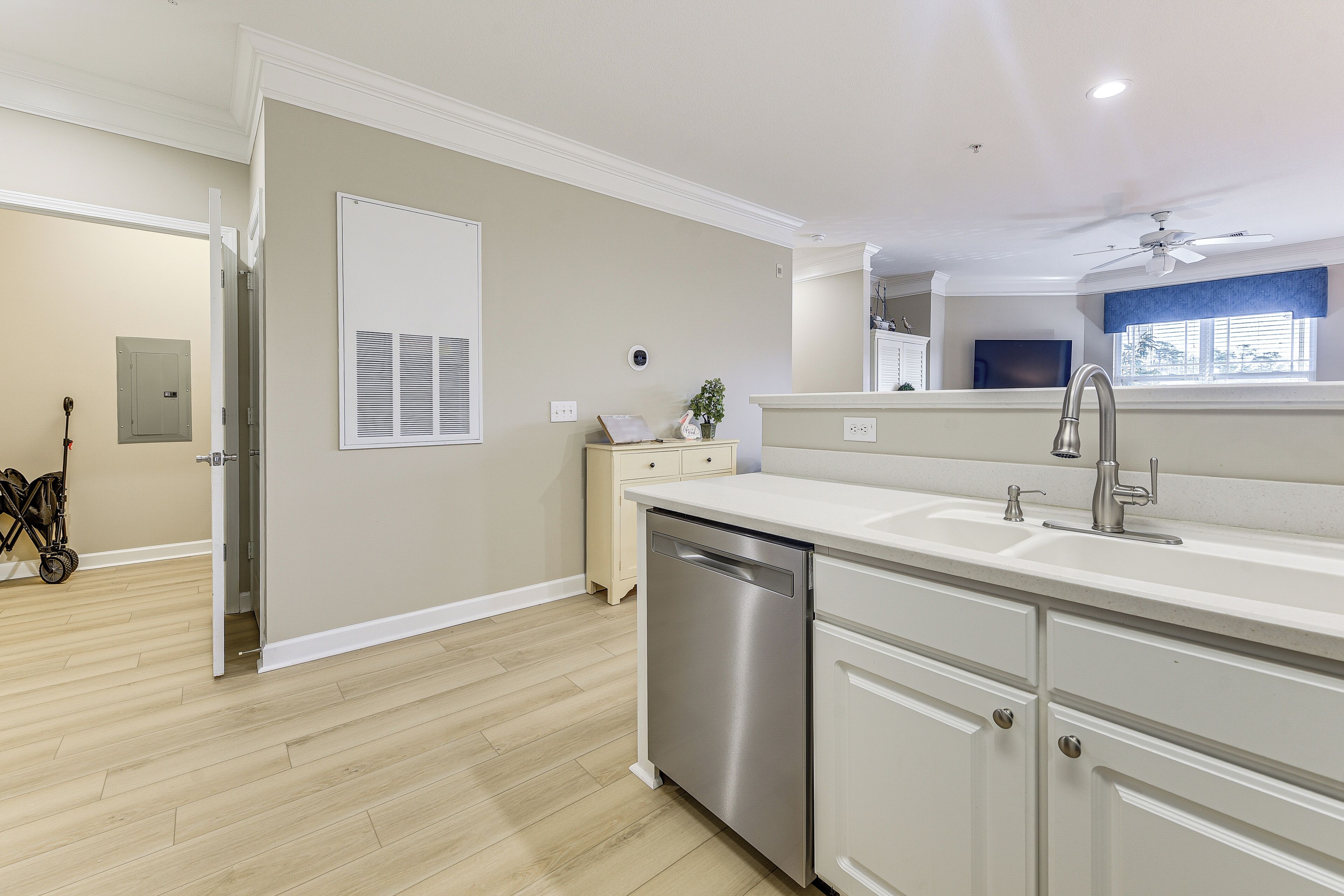 A modern kitchen with a dishwasher, white cabinets, and a window with blinds.