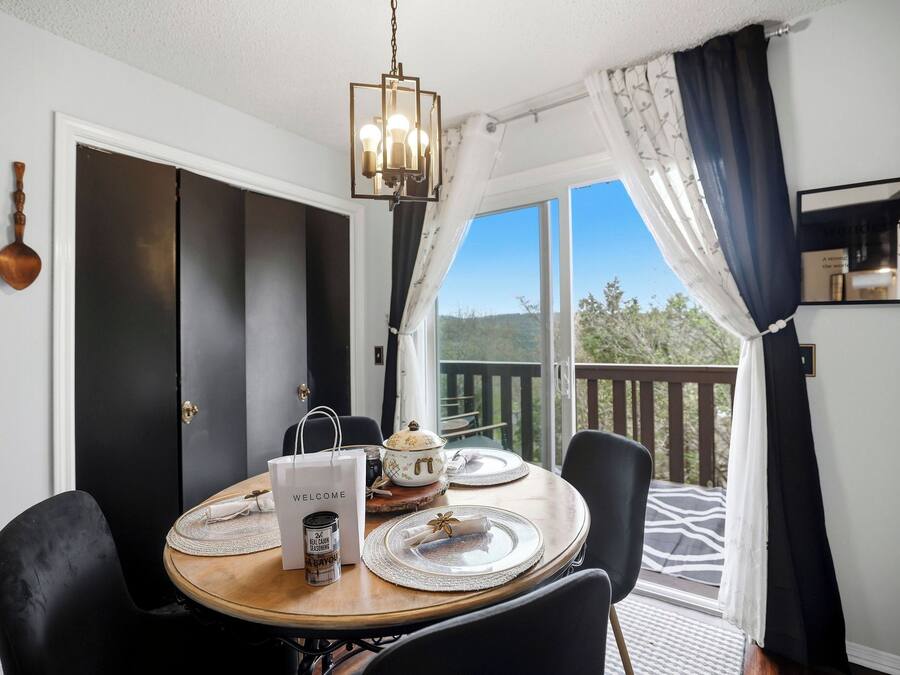 A dining area with a round table, black chairs, a chandelier, and a view of the outdoors.