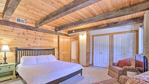 Quarto com teto de madeira, uma cama, mesa de cabeceira, cadeira e guarda-roupa.