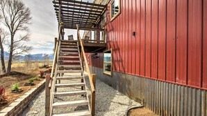 A wooden staircase leading to a balcony with a metal railing, adjacent to a red building with a window and a door.