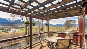 A wooden deck with a table and chairs, overlooking a scenic landscape with mountains and a river.