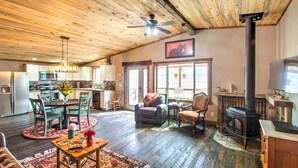 A spacious living area with a large wooden ceiling, a fireplace, and a kitchen in the background.
