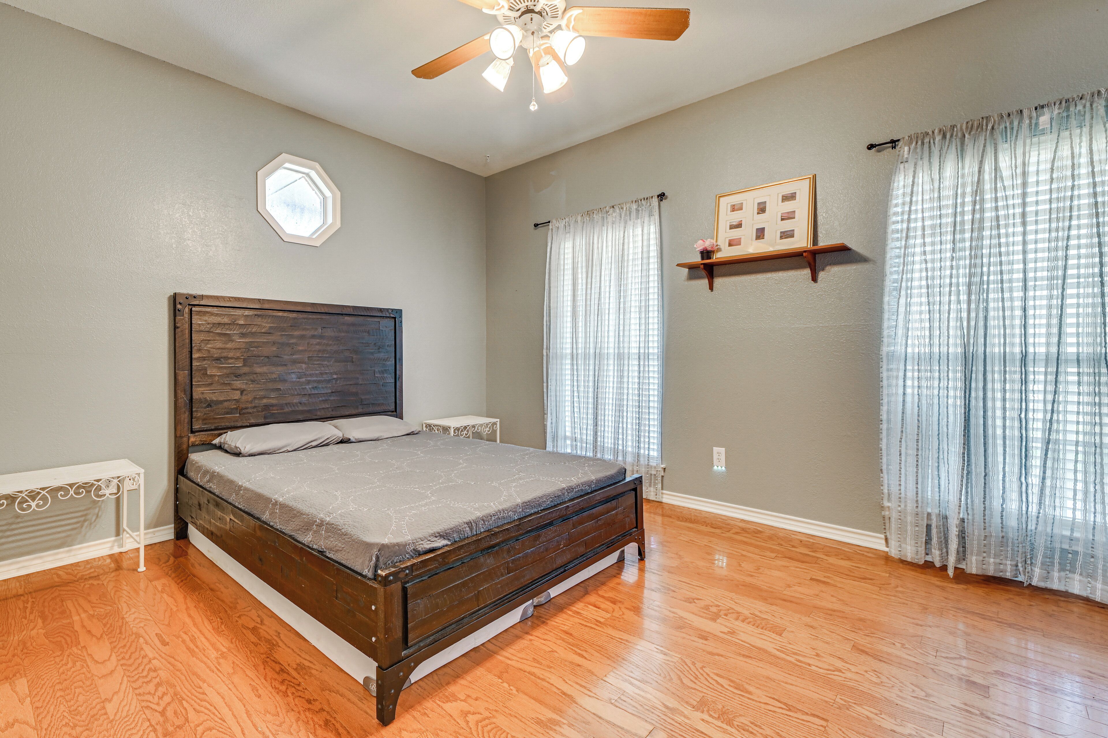 A bedroom with a wooden bed, a ceiling fan, a window with curtains, and a wall-mounted shelf.