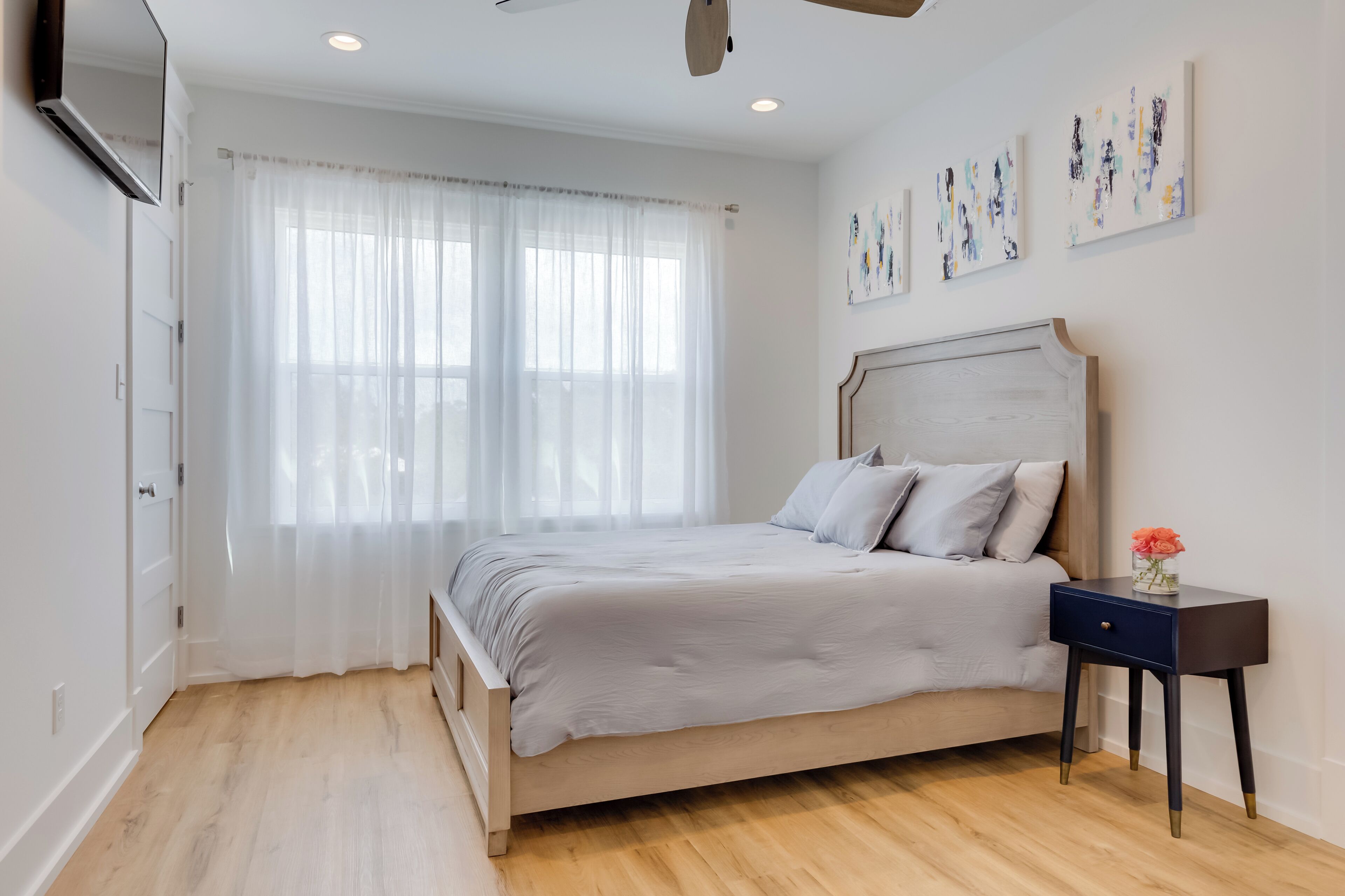 A bedroom with a bed, a nightstand, a wall-mounted TV, and artwork on the wall.