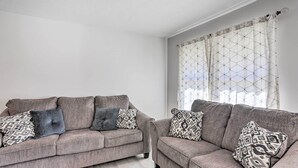 A living room with two grey sofas, patterned cushions, and a window with a geometric curtain. - 5 Mi to UT: Quiet Toledo Duplex Near Parks! (Toledo)