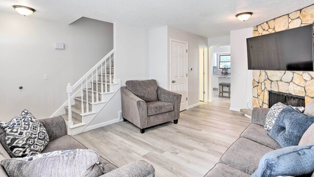 A living room with a grey armchair, a sofa, and a flat-screen TV mounted on a stone wall. - 5 Mi to UT: Quiet Toledo Duplex Near Parks! (Toledo)