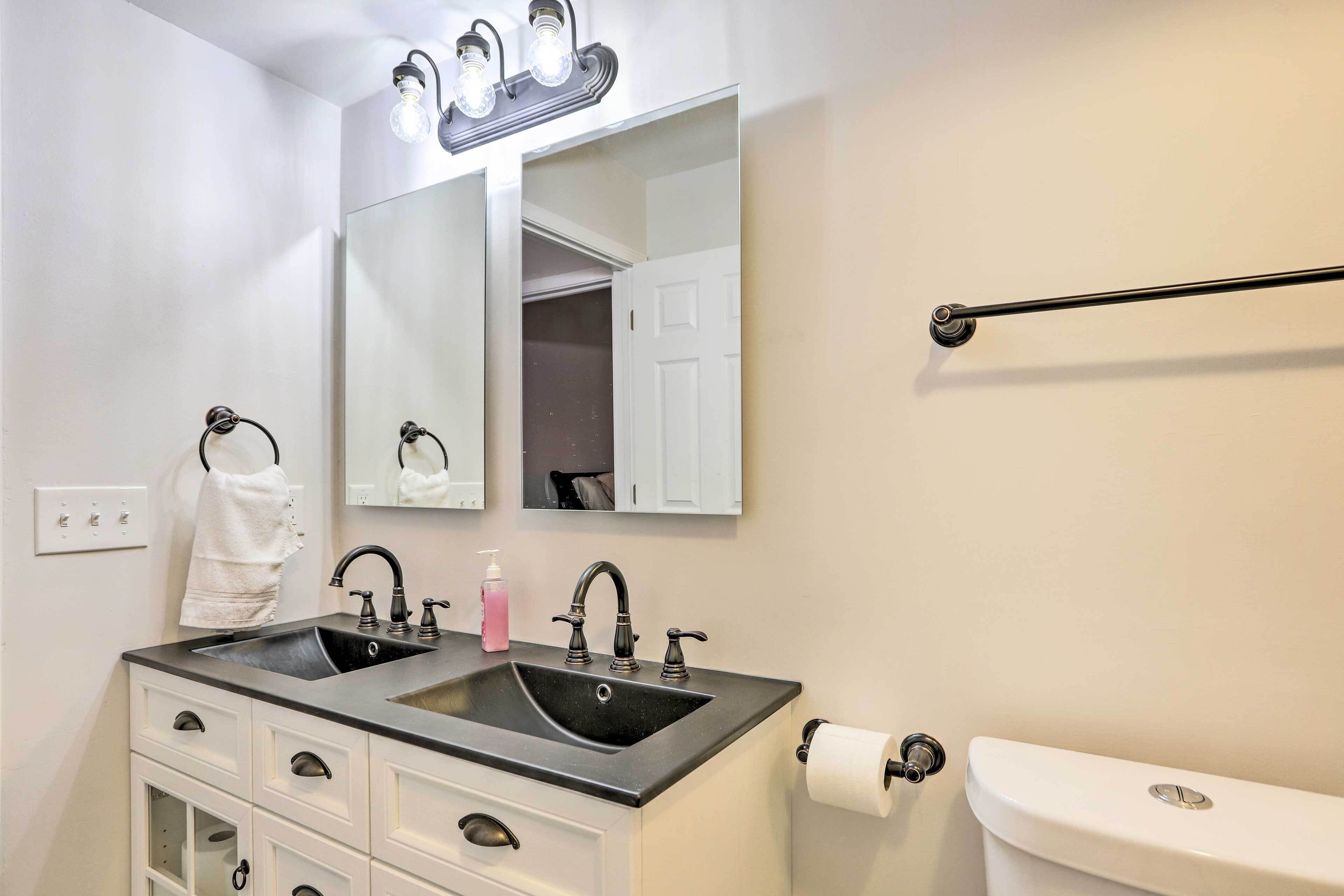 A bathroom with a double sink, a mirror, a towel rack, a toilet, and a towel hanging on the wall.