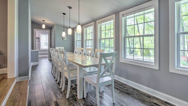 Un espace repas avec une longue table et des chaises, de grandes fenêtres et des luminaires suspendus.