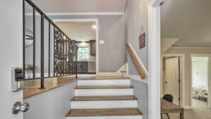 Un escalier avec des marches en bois et une rampe métallique menant à une pièce où se trouvent une table à manger et des chaises.