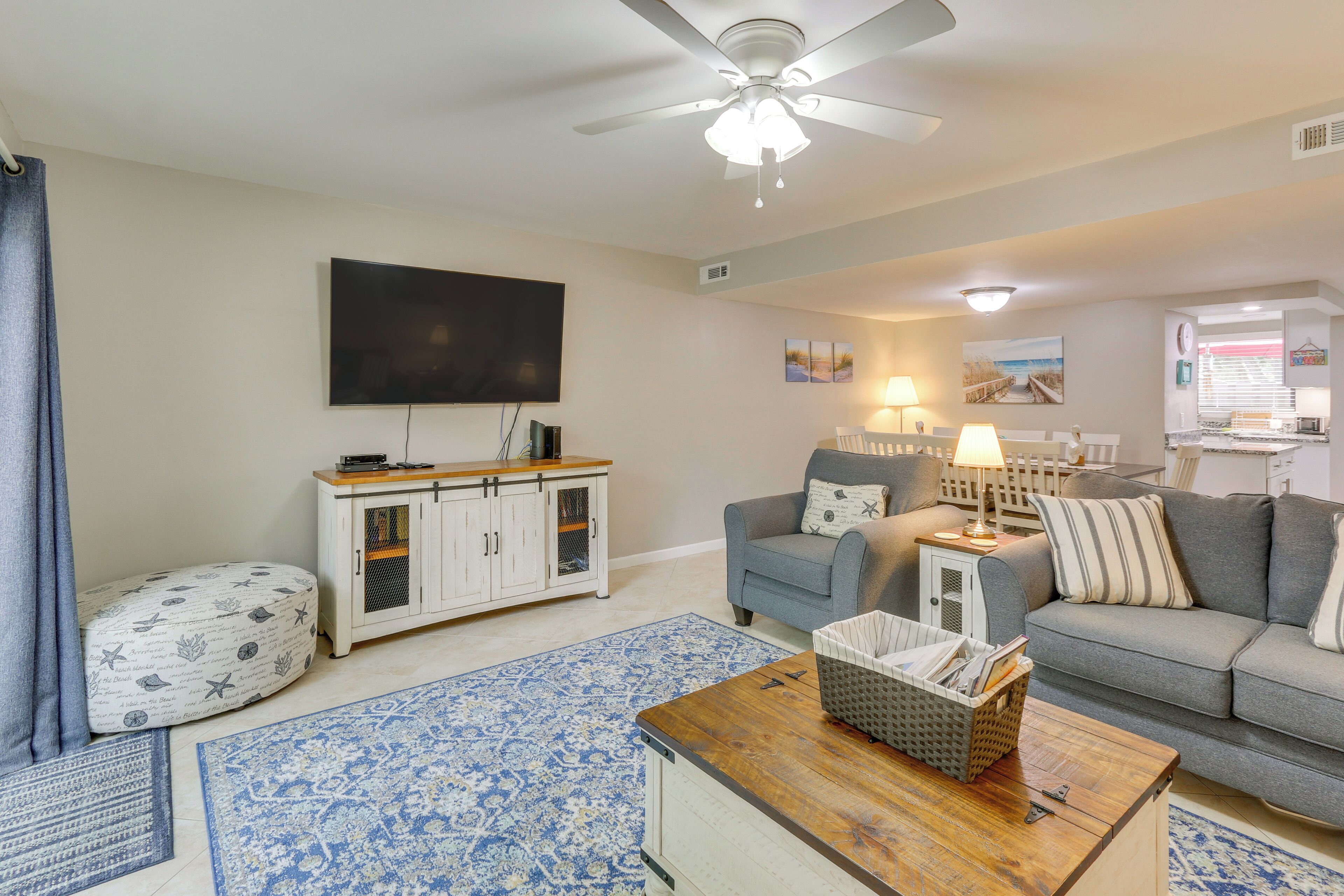 A living room with a ceiling fan, a flat-screen TV, a grey sofa, a wooden coffee table, and a patterned rug.