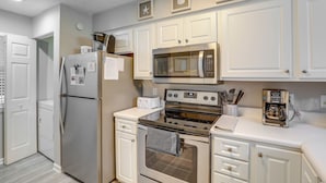 A modern kitchen with white cabinetry, a stainless steel refrigerator, a microwave, a stove, and a coffee maker. - 'southern Charm' Condo w/ Pool ~ 4 Mi to Broadway! (Myrtle Beach)