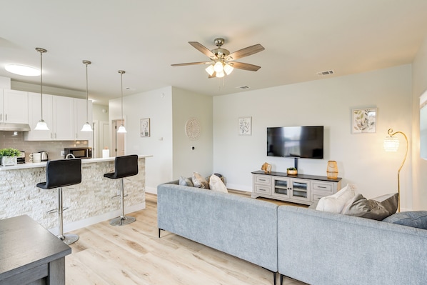 A modern kitchen with a bar area, a grey sofa, and a flat-screen TV. - Steps to TCU Campus: Modern Fort Worth Apt (Fort Worth)