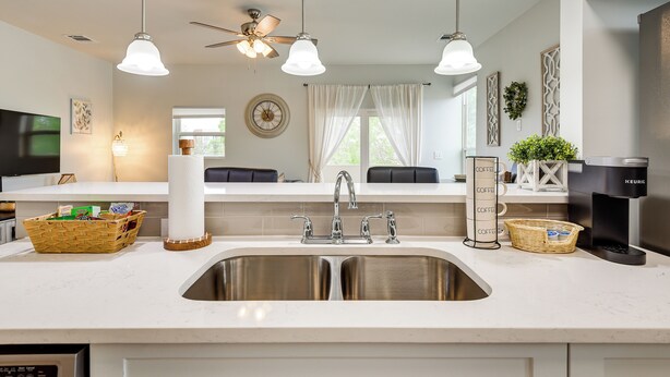 A modern kitchen with a double sink, a ceiling fan, pendant lights, a coffee maker, and wicker baskets.