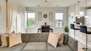 A modern living room with a grey sofa, a ceiling fan, and a kitchen area with bar stools.