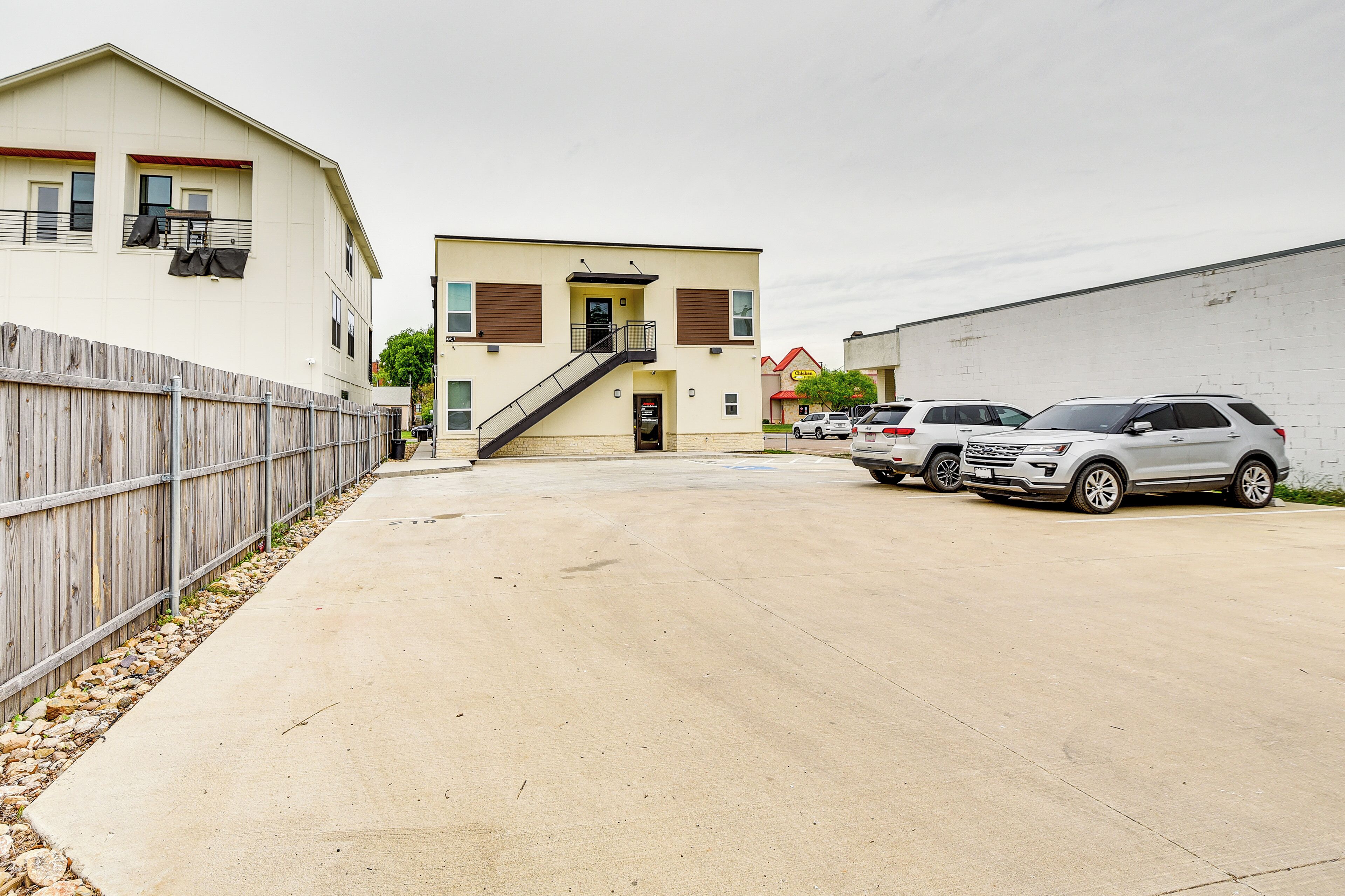 A building with a central staircase, a fenced area, and parked cars.