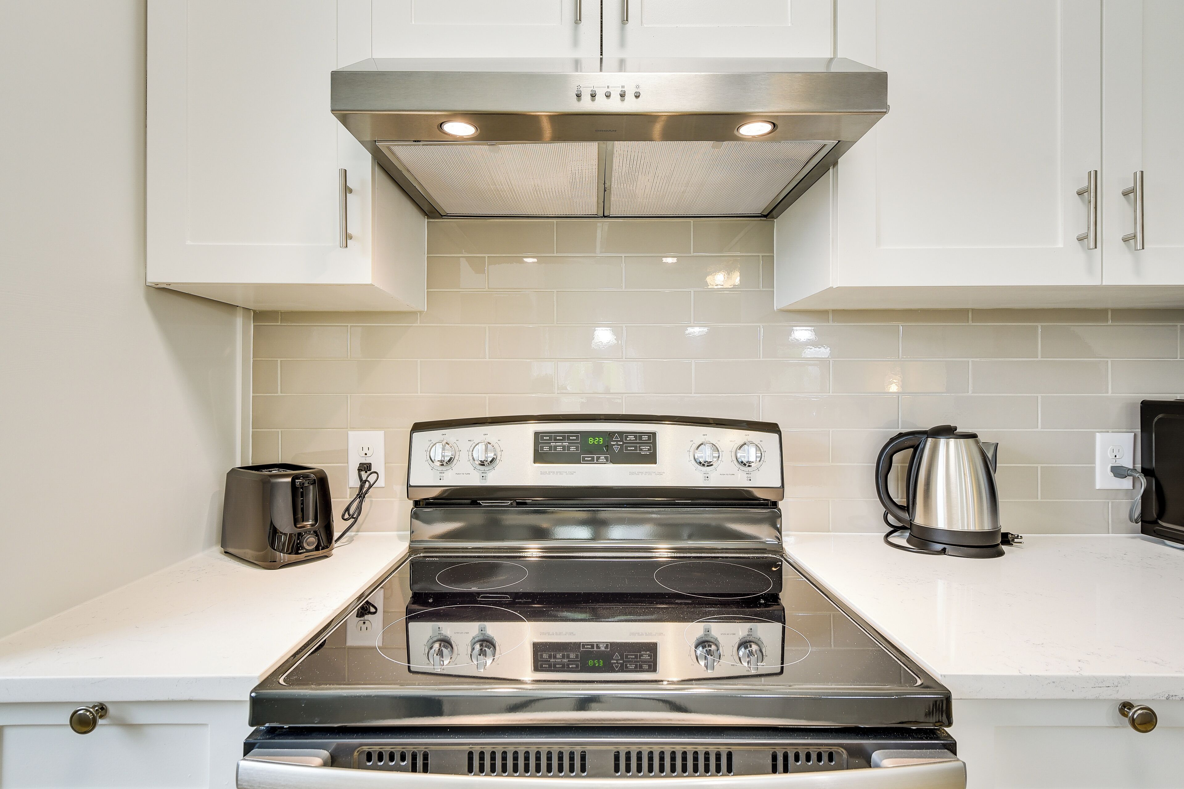 A kitchen with a stainless steel stove, a coffee maker, and a kettle on the counter.