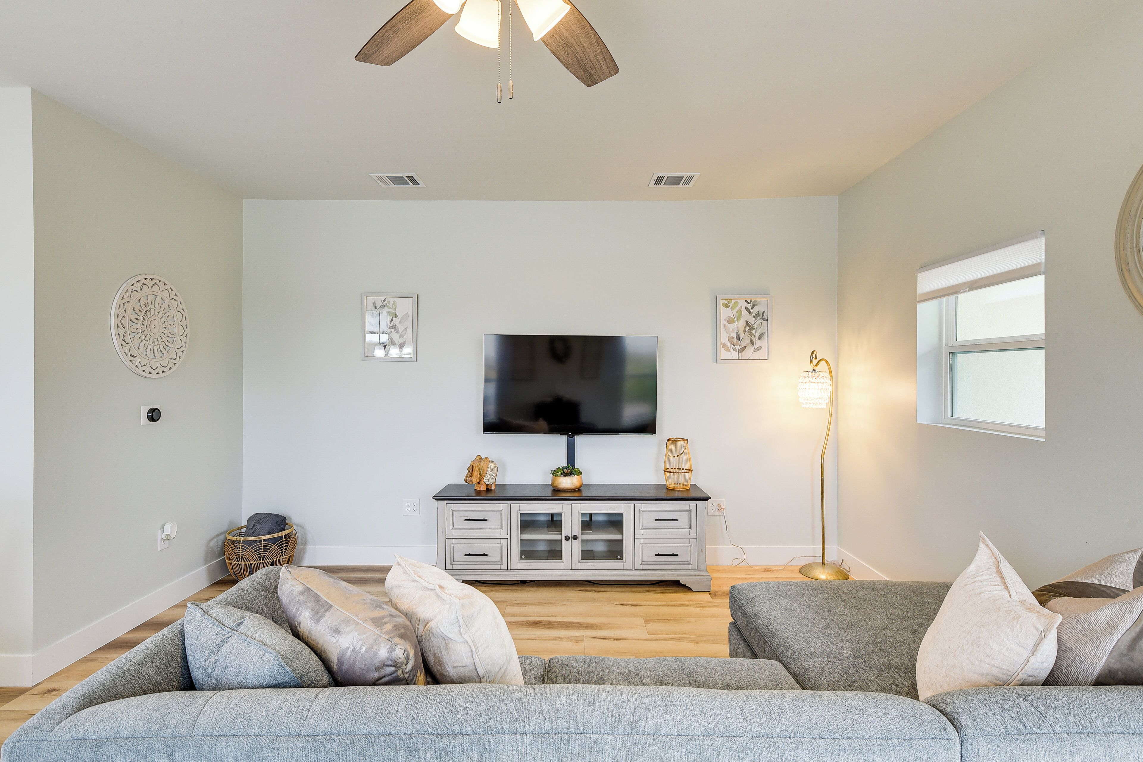 A living room with a grey sofa set, a flat-screen TV on a grey cabinet, a ceiling fan, and a floor lamp.