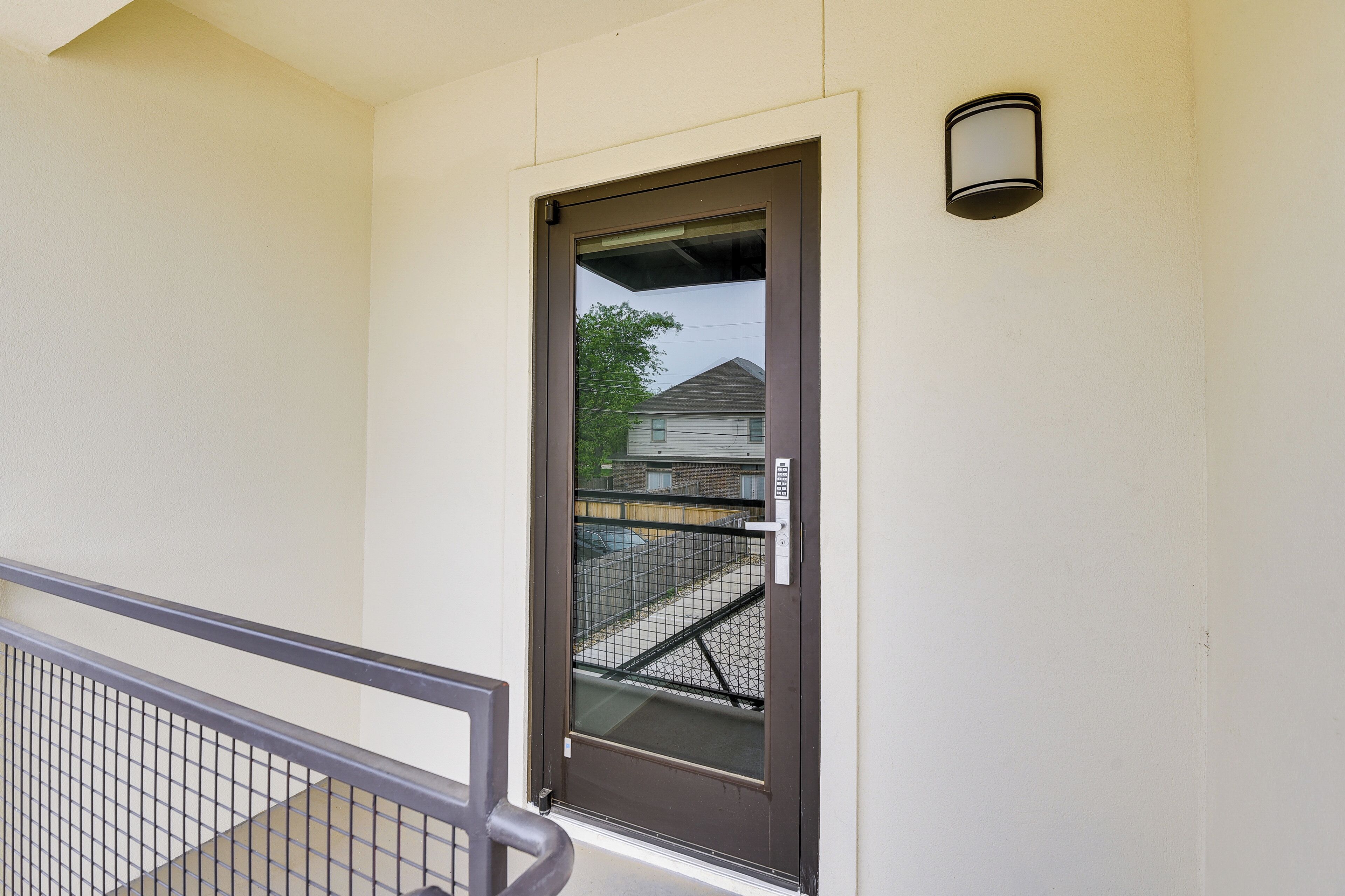 A door with a metal gate, a small outdoor light fixture, and a view of a residential area in the background.