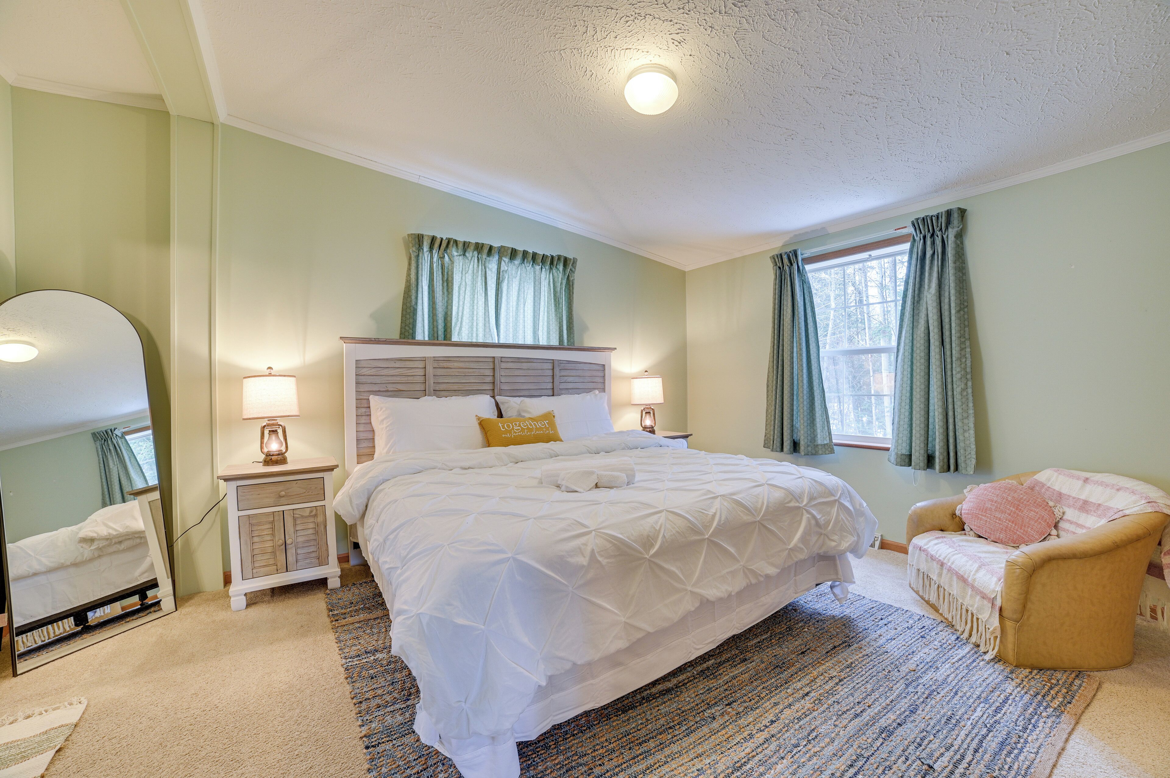 Une chambre à coucher avec un grand lit, une table de chevet avec une lampe, une chaise et une fenêtre avec des rideaux.