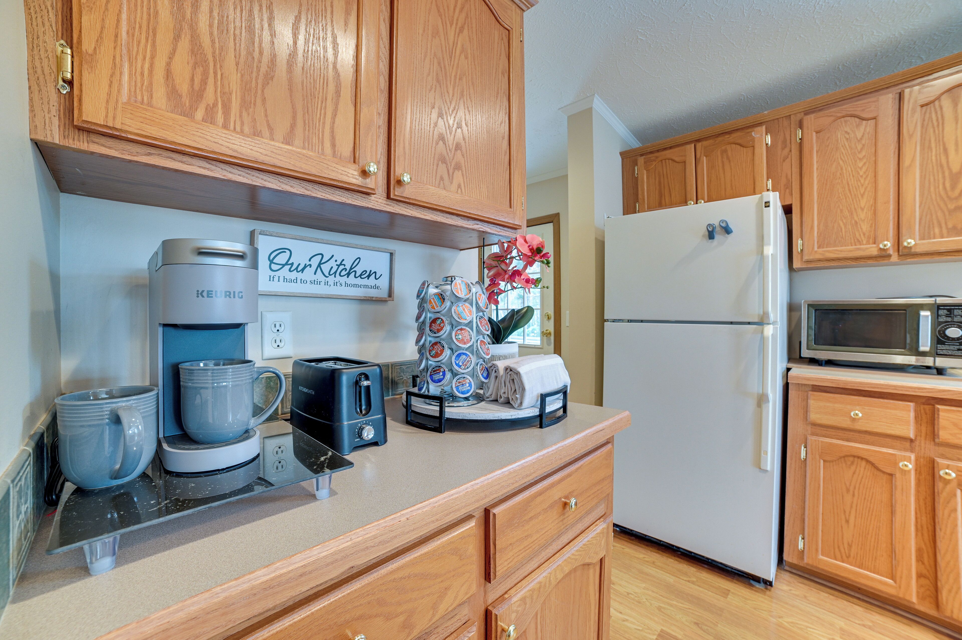 A kitchen with wooden cabinets, a coffee maker, a toaster, a refrigerator, and a microwave.