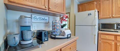 A kitchen with wooden cabinets, a coffee maker, a toaster, a refrigerator, and a microwave.