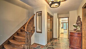 A wooden staircase leading to a landing, a door with a mirror, and a stone-tiled floor.
