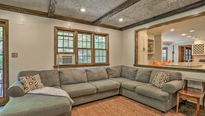 A living room with a sectional sofa, a small wooden side table, and a large mirror reflecting the kitchen area.