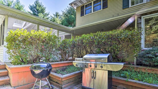A backyard with a stainless steel grill and a barbecue grill, surrounded by a brick patio and greenery.