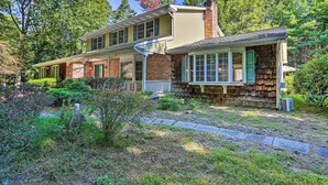 A two-story house with a brick facade, a covered porch, and a stone pathway leading to the entrance.
