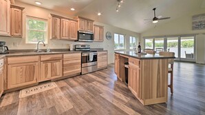 Une cuisine spacieuse avec des meubles en bois, un grand îlot central, des appareils électroménagers en acier inoxydable et une vue sur l’extérieur.