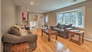 A spacious living room with hardwood flooring, a grey sofa, a coffee table, and a side table with a book. - Family-friendly Woodbury Home With Yard + Deck! (Woodbury)