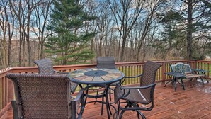 A wooden deck with a round glass table and wicker chairs, surrounded by trees. - Family-friendly Woodbury Home With Yard + Deck! (Woodbury)